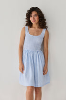 Smocked Short Dress in Blue Stripes designed with a fitted textured bodice and airy striped skirt, creating a timeless casual-chic outfit. 