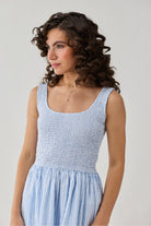 Woman wearing a light blue striped smocked dress with a fitted bodice and soft gathered skirt, styled with natural curls.
