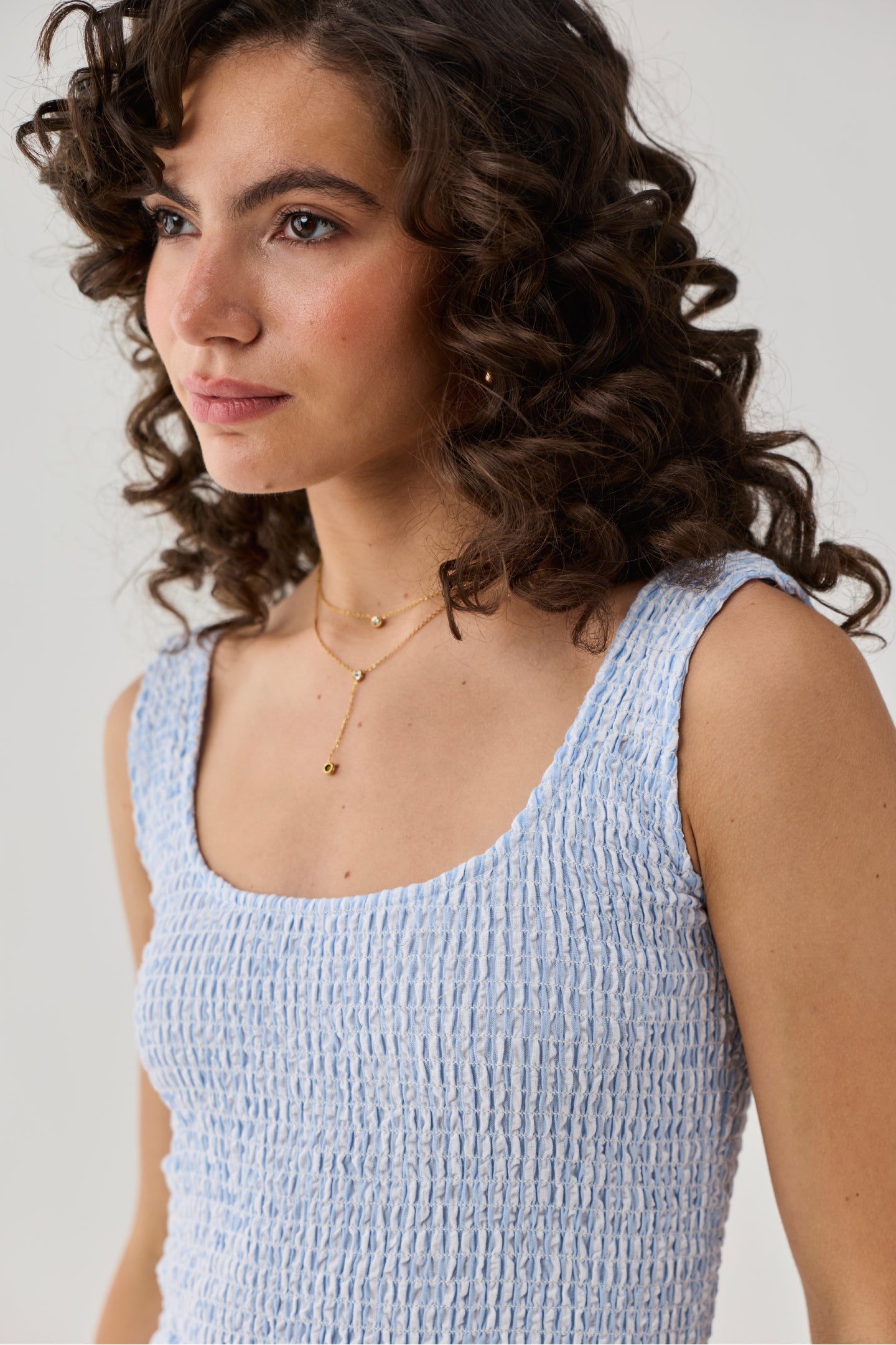 Close-up of a woman wearing a blue striped smocked dress with a textured bodice, sleeveless design, and soft summer-inspired style.