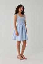 Fashion model showcasing a blue striped smocked short dress with a square neckline and airy skirt in a minimalist studio setting.