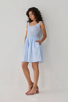 Lightweight blue striped sleeveless dress with gathered detailing and side pockets, offering a feminine and versatile seasonal outfit. 