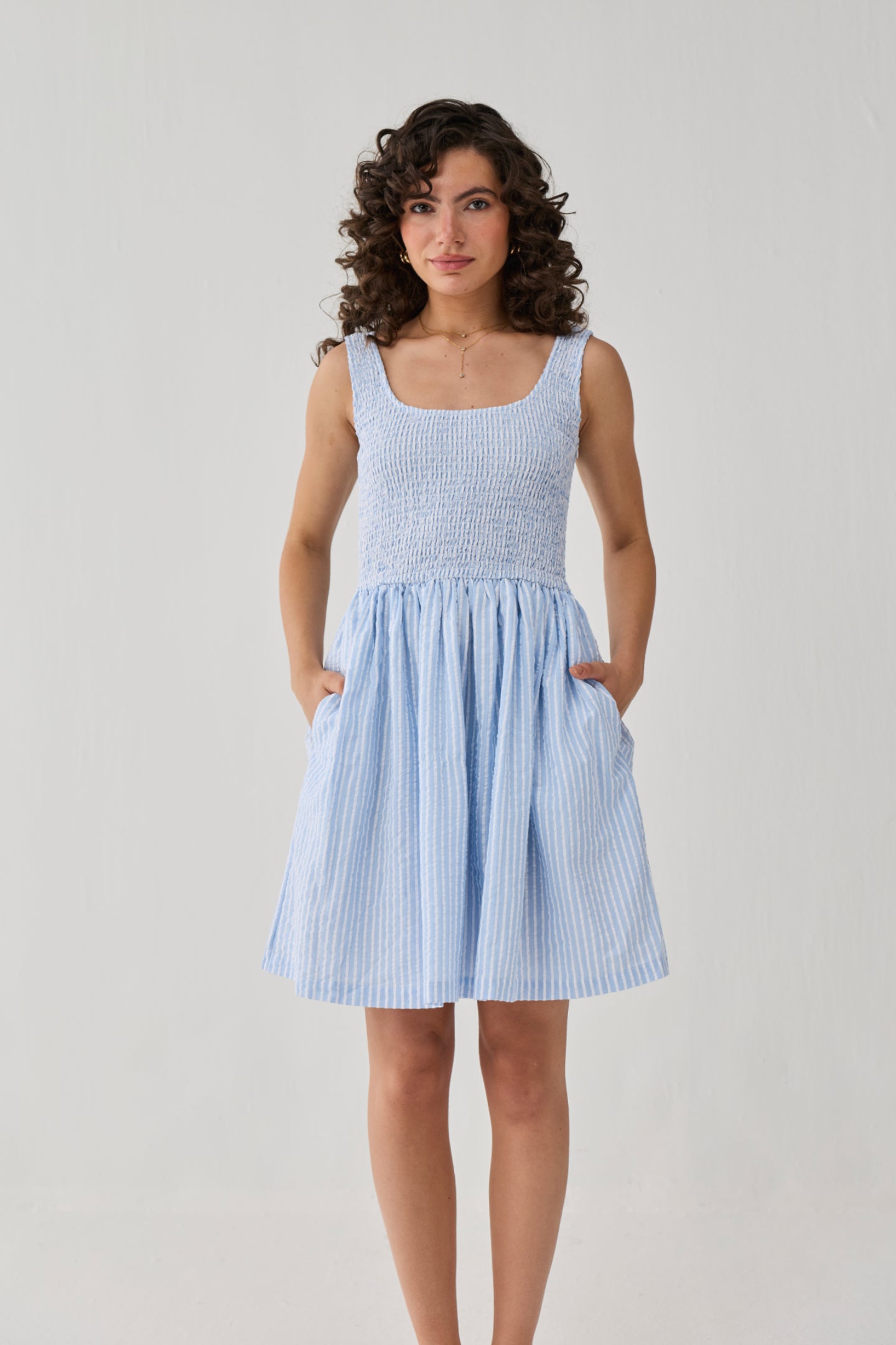 Smocked Short Dress in Blue Stripes with a flattering fit-and-flare silhouette, sleeveless design, and practical pockets for everyday wear.