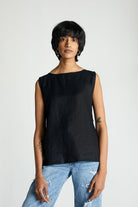 A woman wearing a sleeveless black top with eyelet buttons at the back, paired with blue jeans.