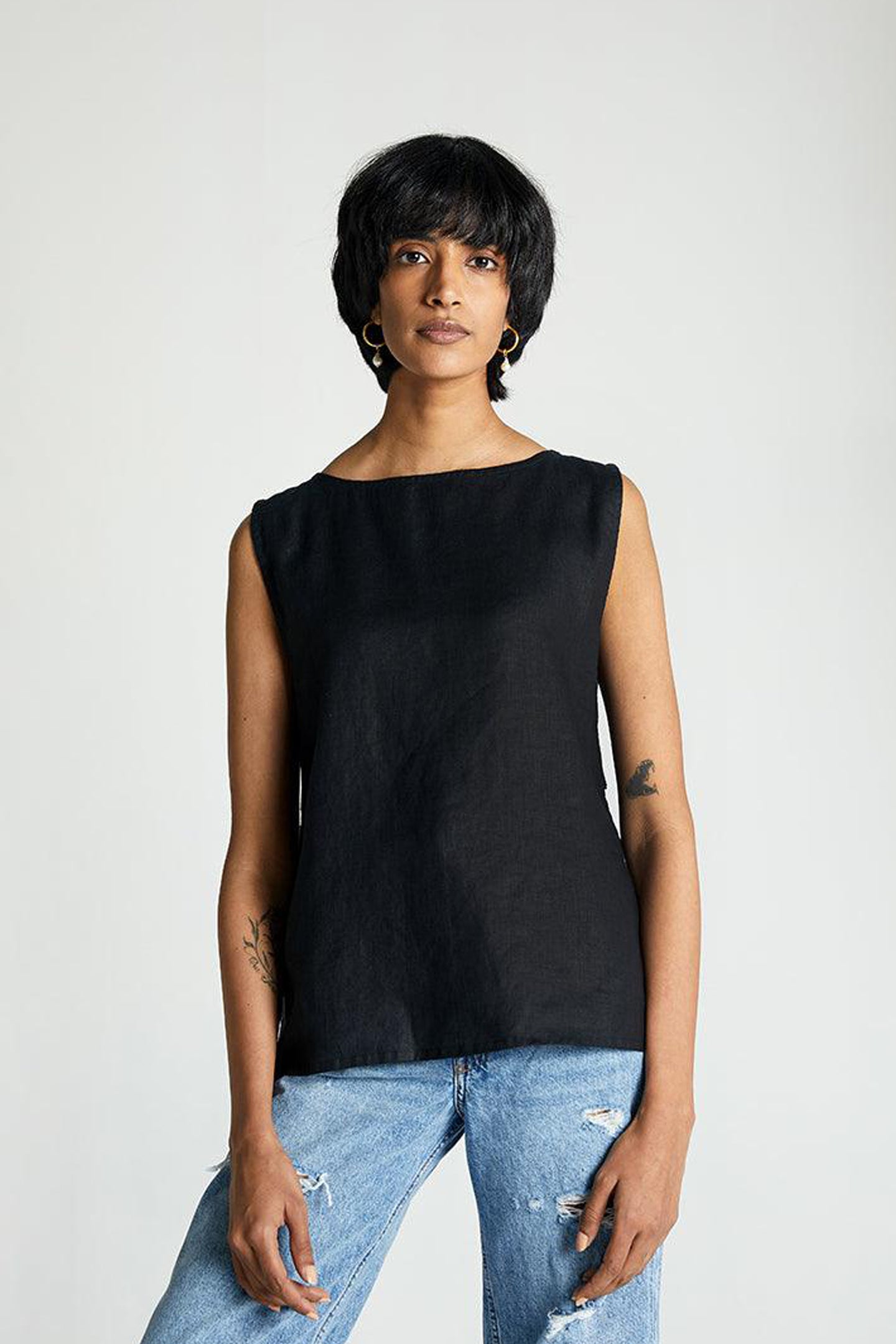 A woman wearing a sleeveless black top with eyelet buttons at the back, paired with blue jeans.
