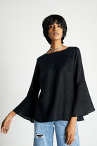 A woman wearing a black bell sleeve shirt with button back detailing over ripped jeans.
