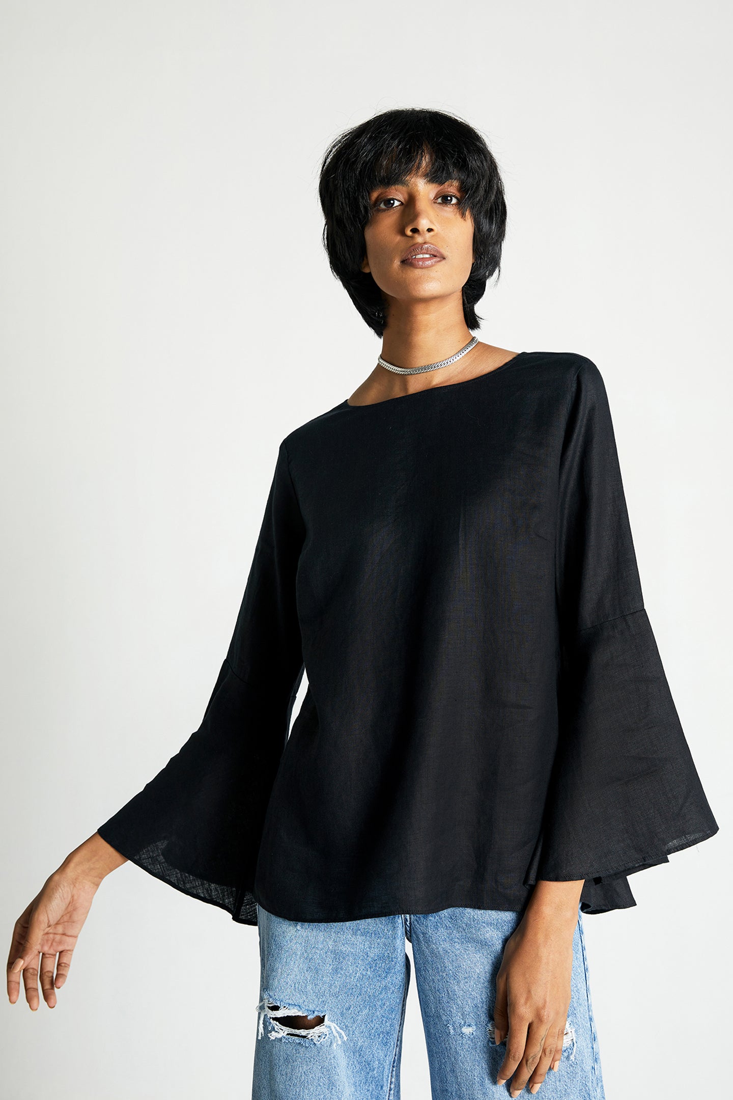 A woman wearing a black bell sleeve shirt with button back detailing over ripped jeans.