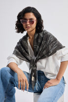The Mara Scarf in Black styled over a white top with blue jeans, worn by a model with sunglasses.
