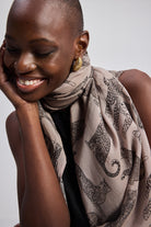 A woman wearing The Mara Scarf in Brown with a neutral background – Reistor.