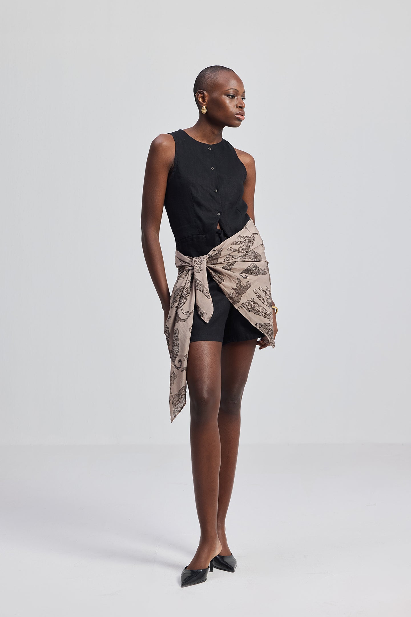 Woman wearing a black sleeveless top and patterned wrap skirt on a white background, featuring The Mara Scarf in Brown by Reistor.
