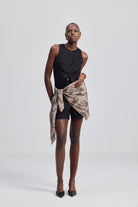Woman wearing a black sleeveless top and shorts styled with The Mara Scarf in Brown by Reistor on a white background.