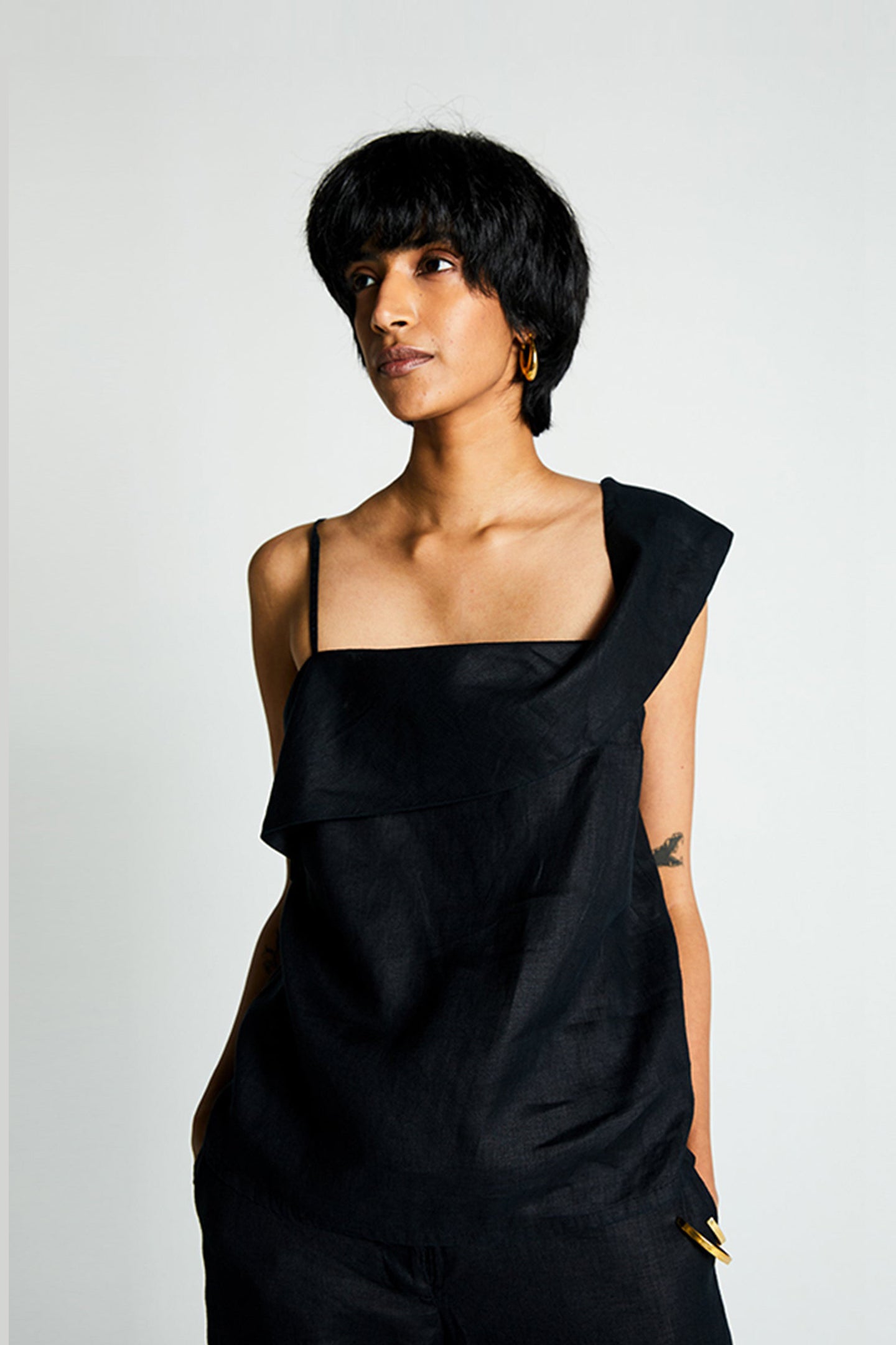 A woman wearing a black one-shoulder sleeveless top with an adjustable strap.