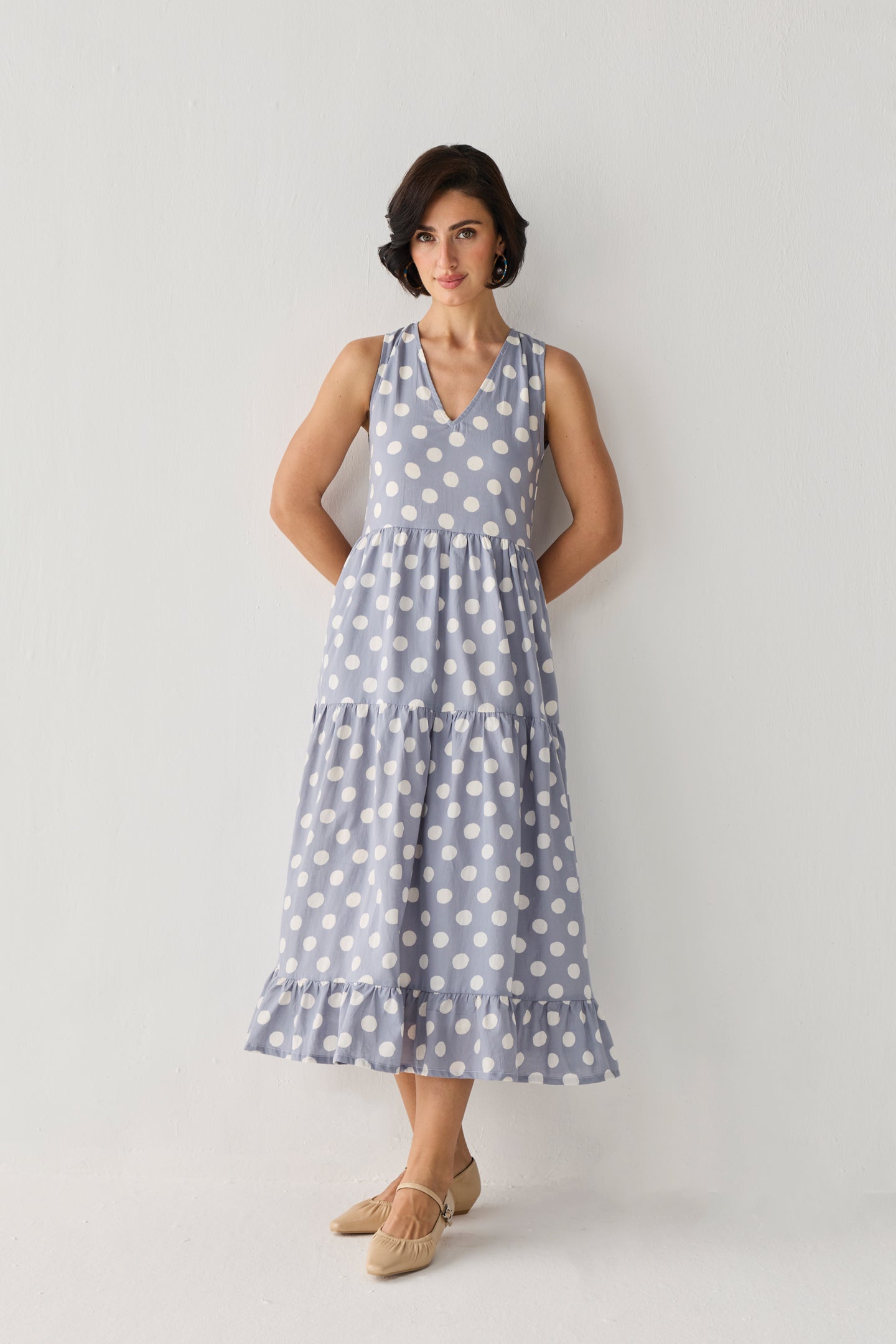 Tiered Midi Dress in Blue Polka featuring a sleeveless design, V-neckline, and flowing tiered skirt with white polka dots, shown in a full-length studio portrait.