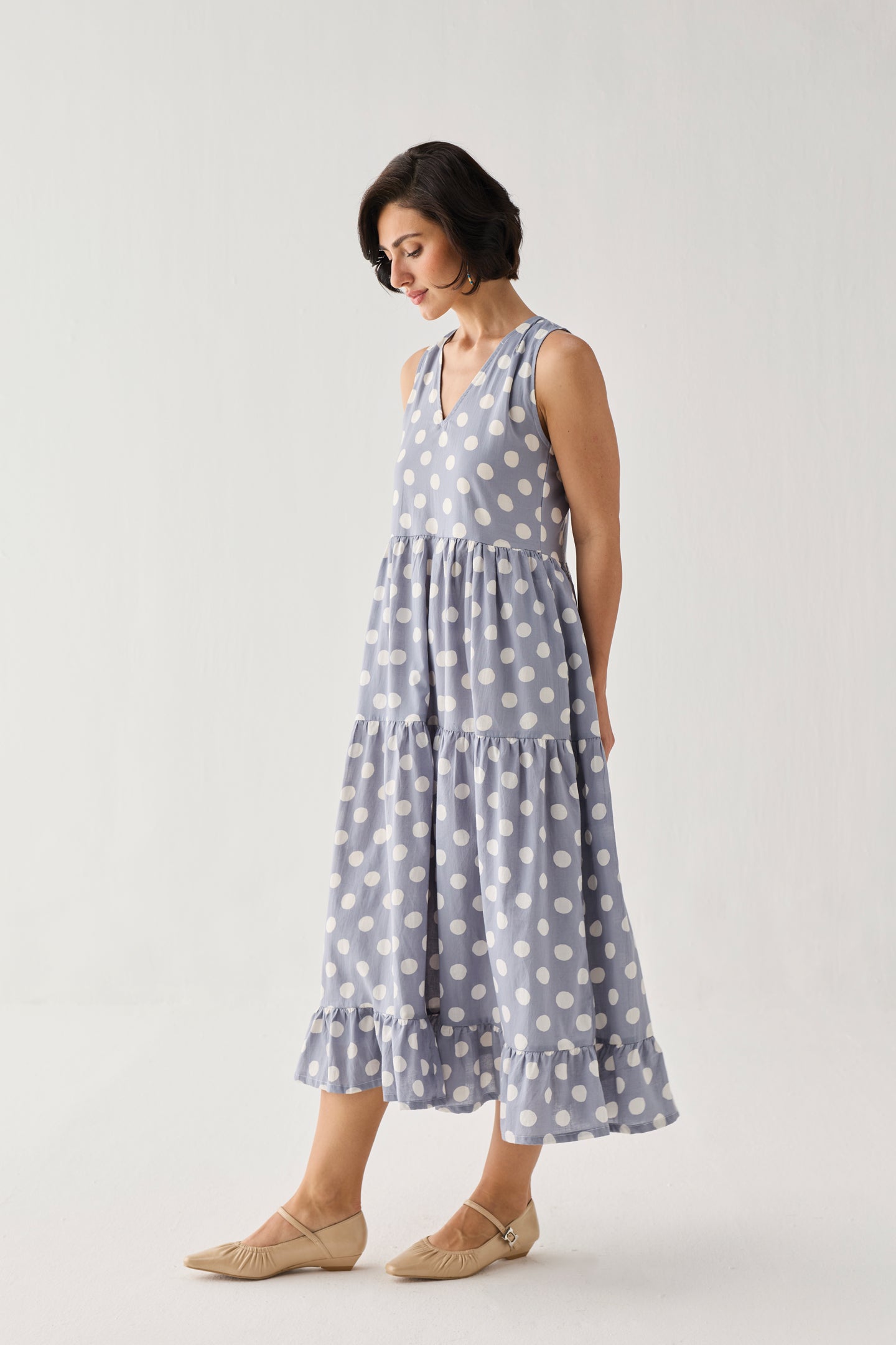 Tiered Midi Dress in Blue Polka featuring a sleeveless design, V-neckline, and flowing tiered skirt with white polka dots, shown in a side studio view.