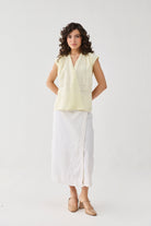 Woman wearing a light yellow sleeveless top and white pants on a white background