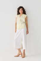 Model wearing Reistor's V-neck Overlap Top in Butter Lemon, styled with a white midi skirt and beige block heels for an effortless, elegant look.