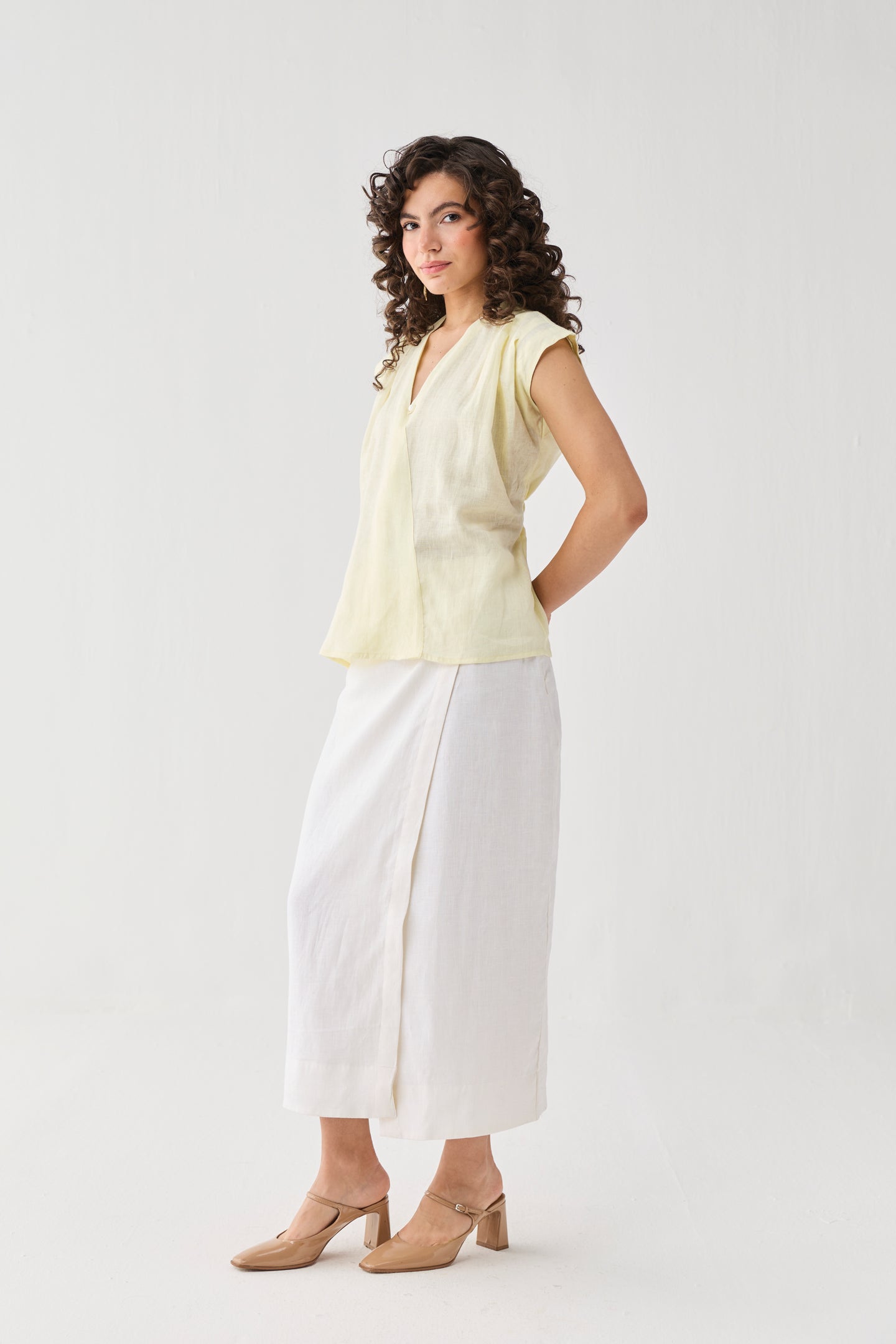 Reistor V-neck Overlap Top in Butter Lemon styled with a white midi skirt and beige heels, captured in a three-quarter pose with an effortless silhouette.