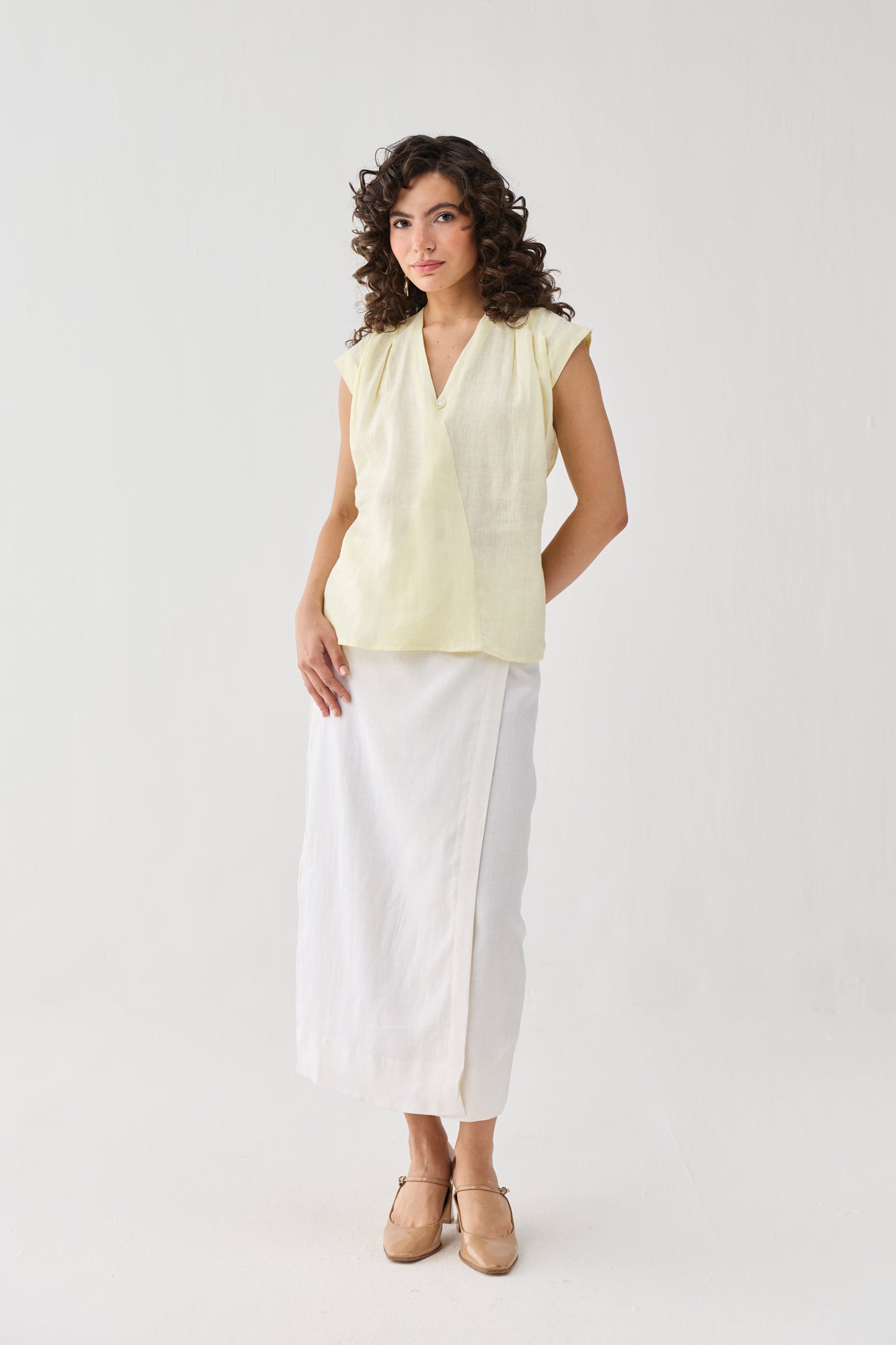 Model wearing Reistor's V-neck Overlap Top in Butter Lemon, styled with a white midi skirt and block heels, highlighting its relaxed fit and elegant overlap neckline.