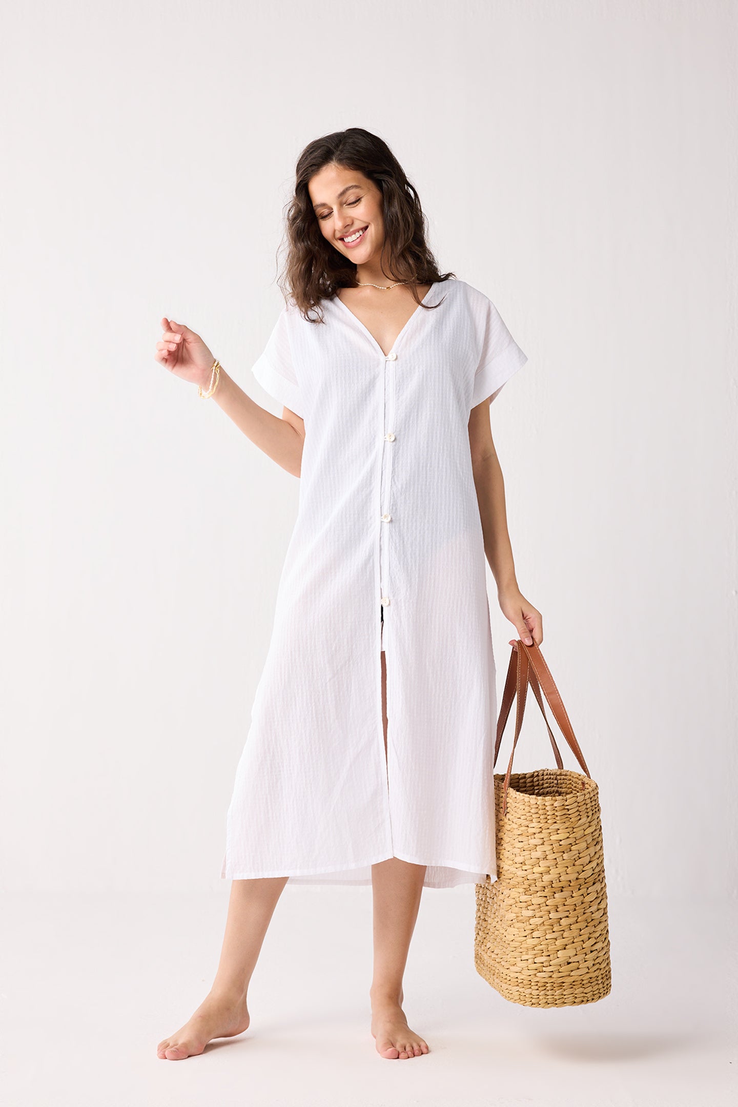 Woman wearing a white dress holding a straw bag on a white background