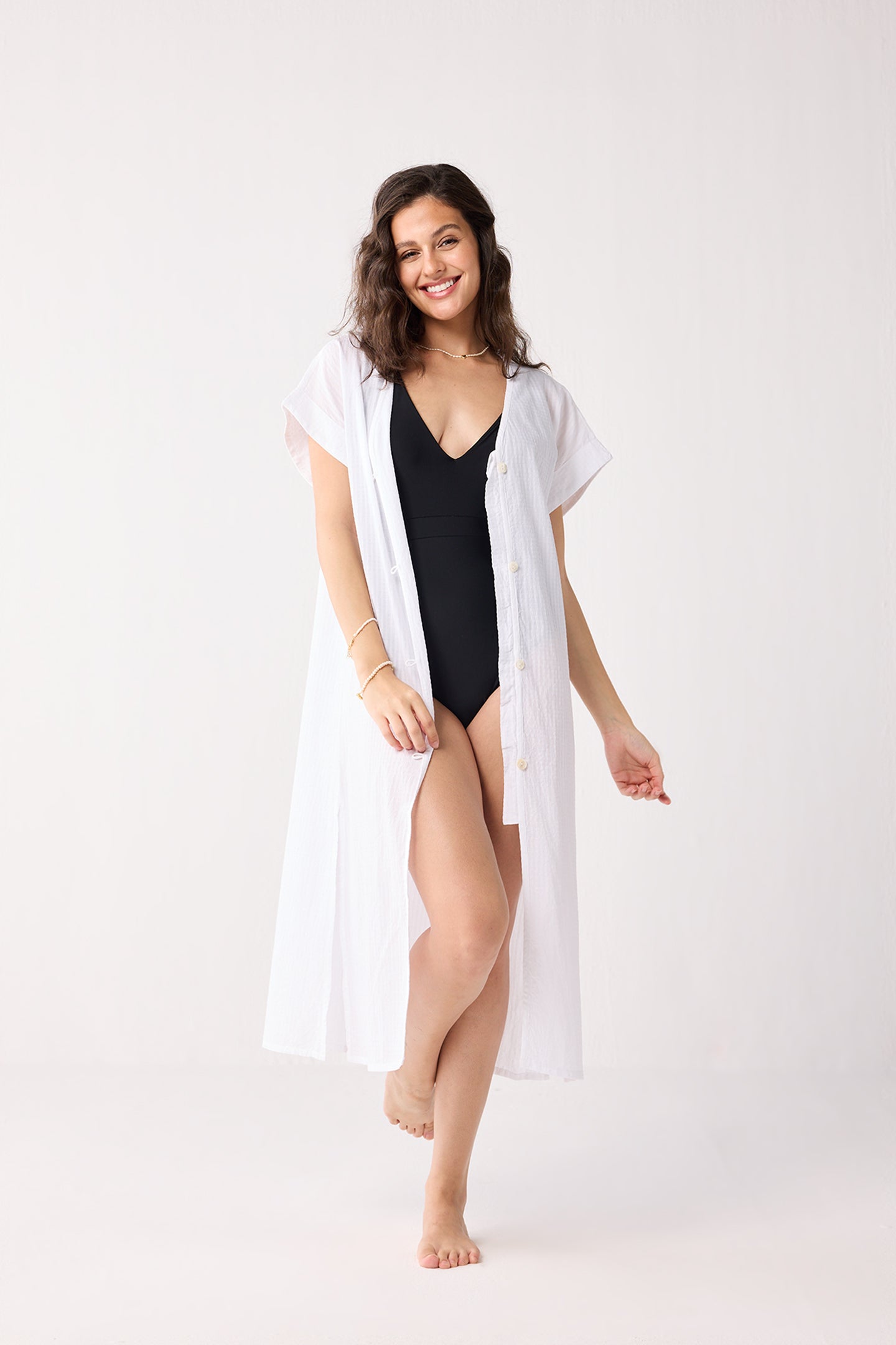 Woman wearing a black swimsuit with a white cover-up on a white background