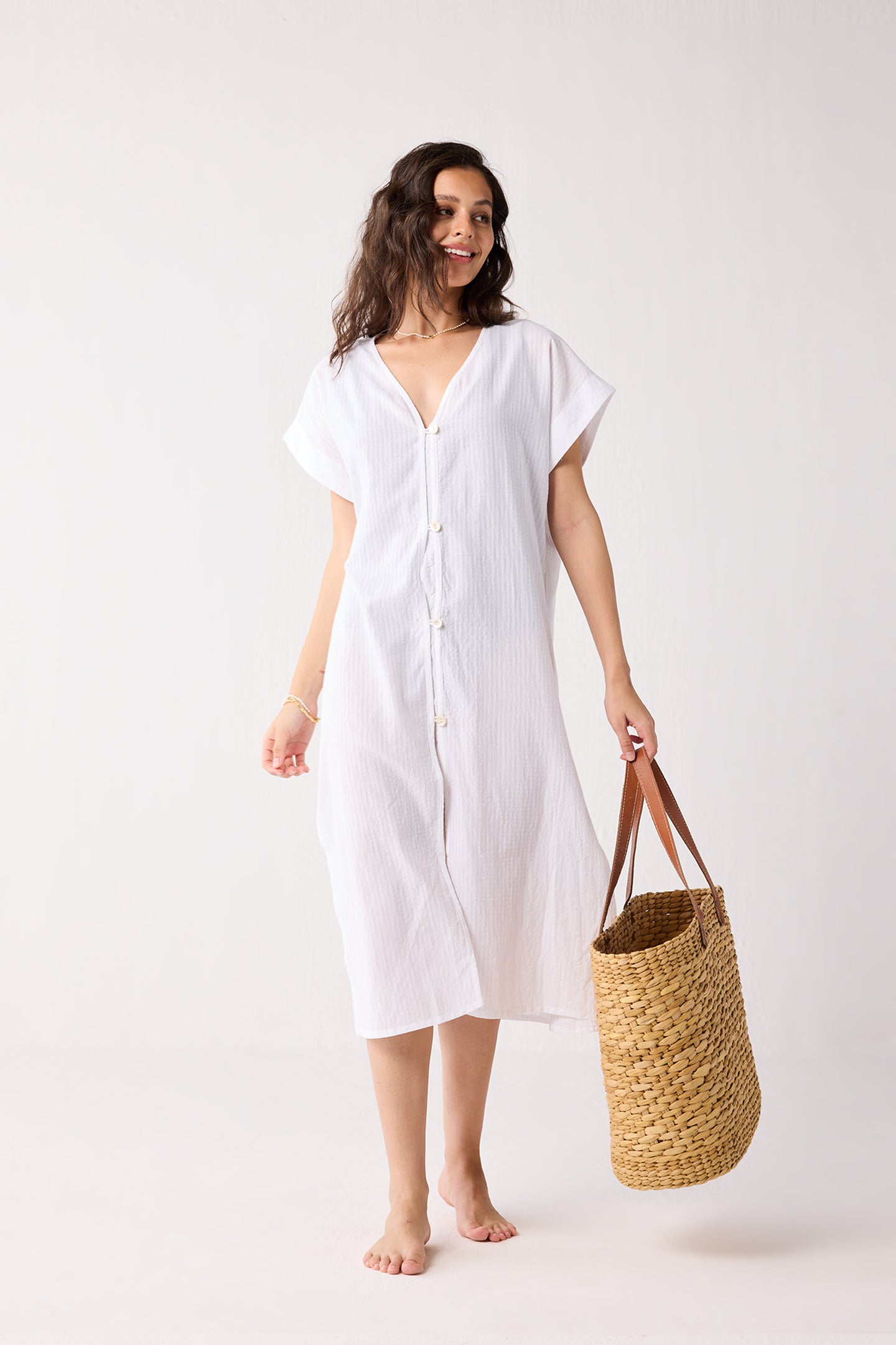 A woman wearing a white dress holding a woven bag on a white background