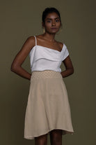 Woman wearing a Reistor white top and beige skirt against a brown background.