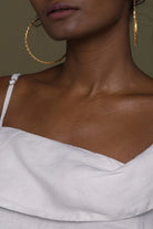 Close-up of a person wearing Reistor gold hoop earrings and a white top.