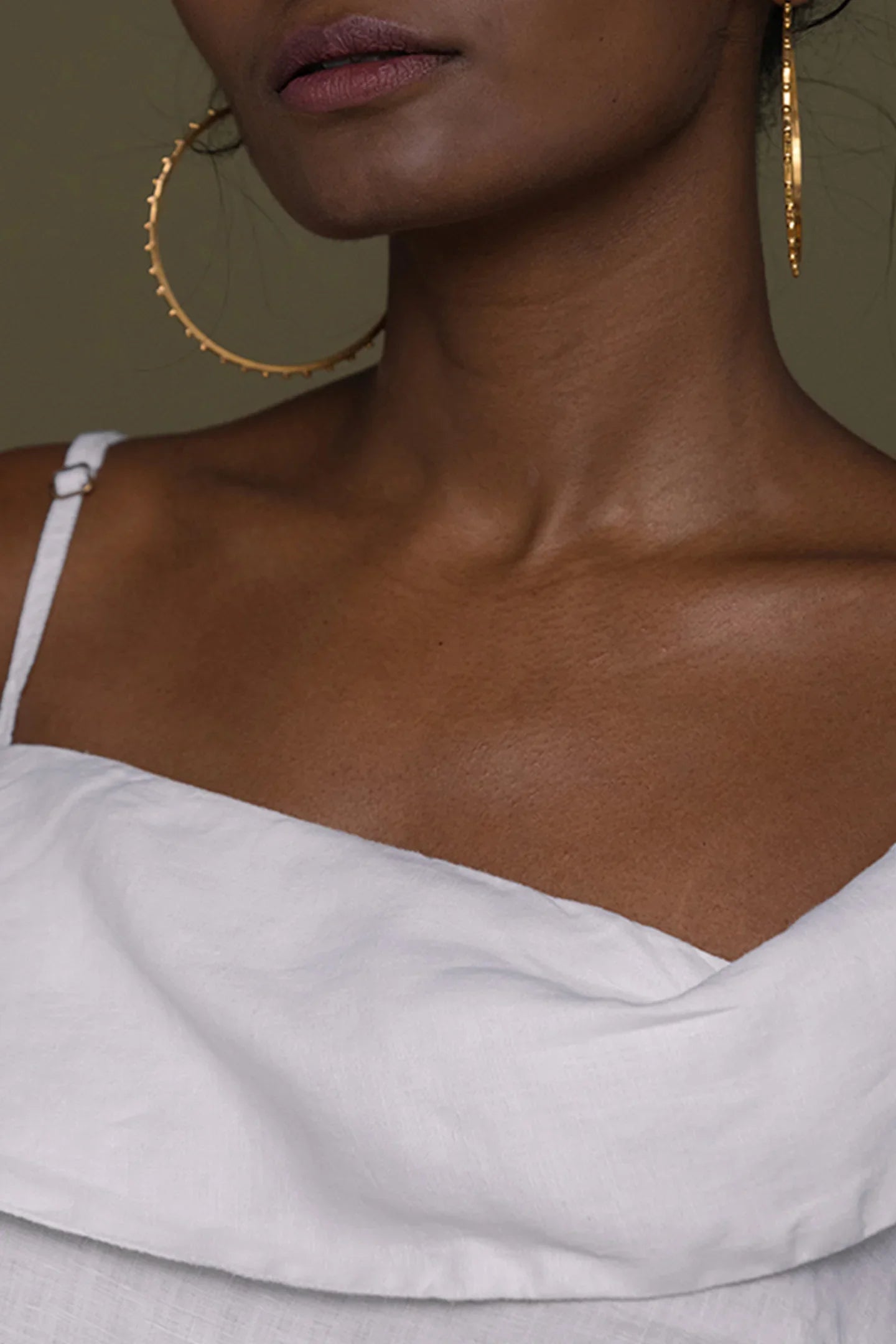 Close-up of a person wearing Reistor gold hoop earrings and a white top.