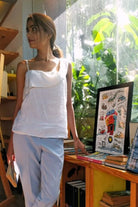 Woman wearing a Reistor white top and light blue pants, standing in a room with books and a framed picture.