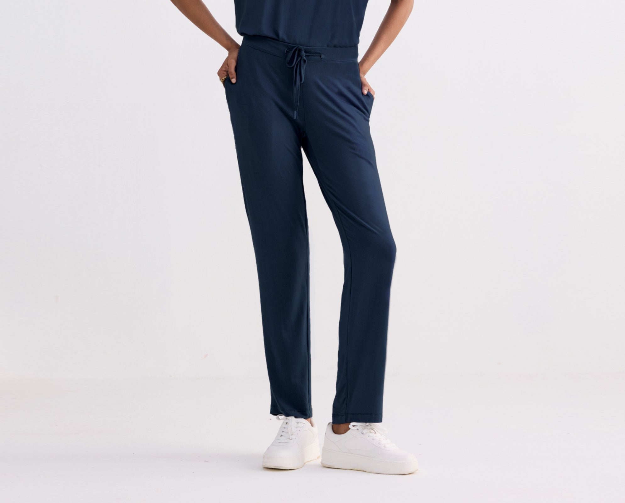Person wearing navy blue pants and white shoes on a light gray background