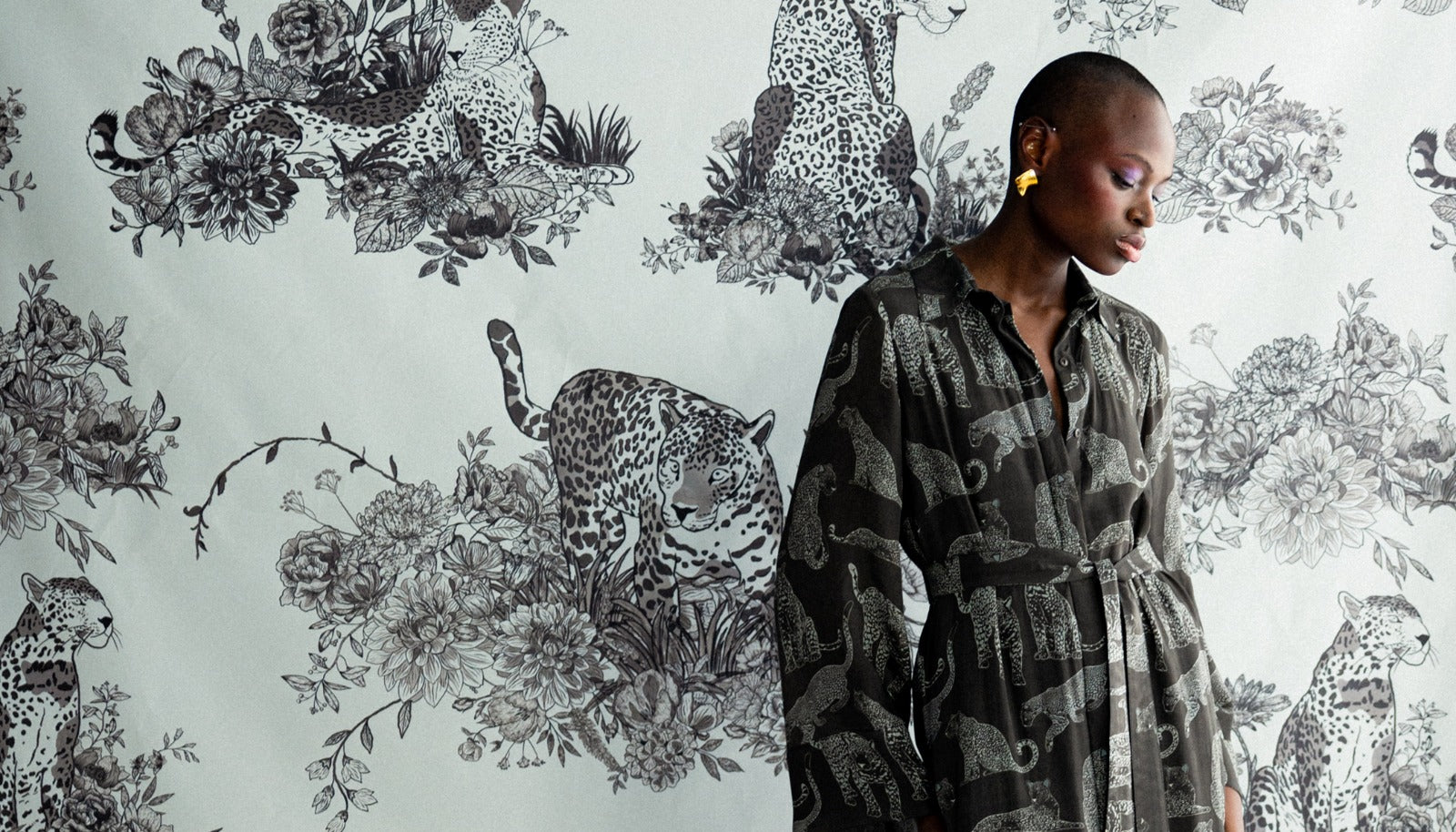 Woman in a patterned dress standing against a wallpaper with leopards and flowers