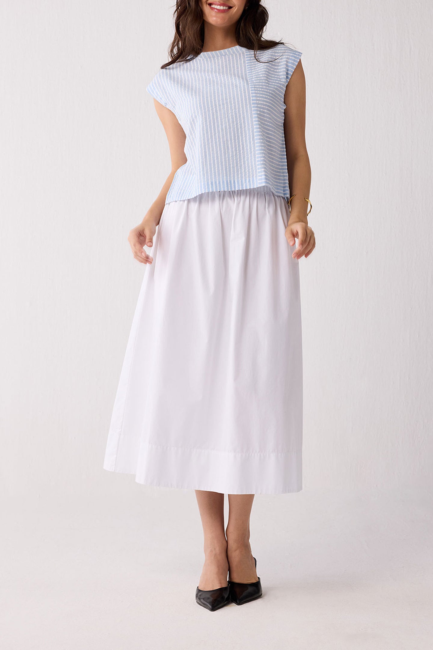 A woman wearing a light blue striped top and a white skirt on a plain background