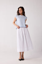 A woman wearing a light blue striped top and a white skirt on a plain background