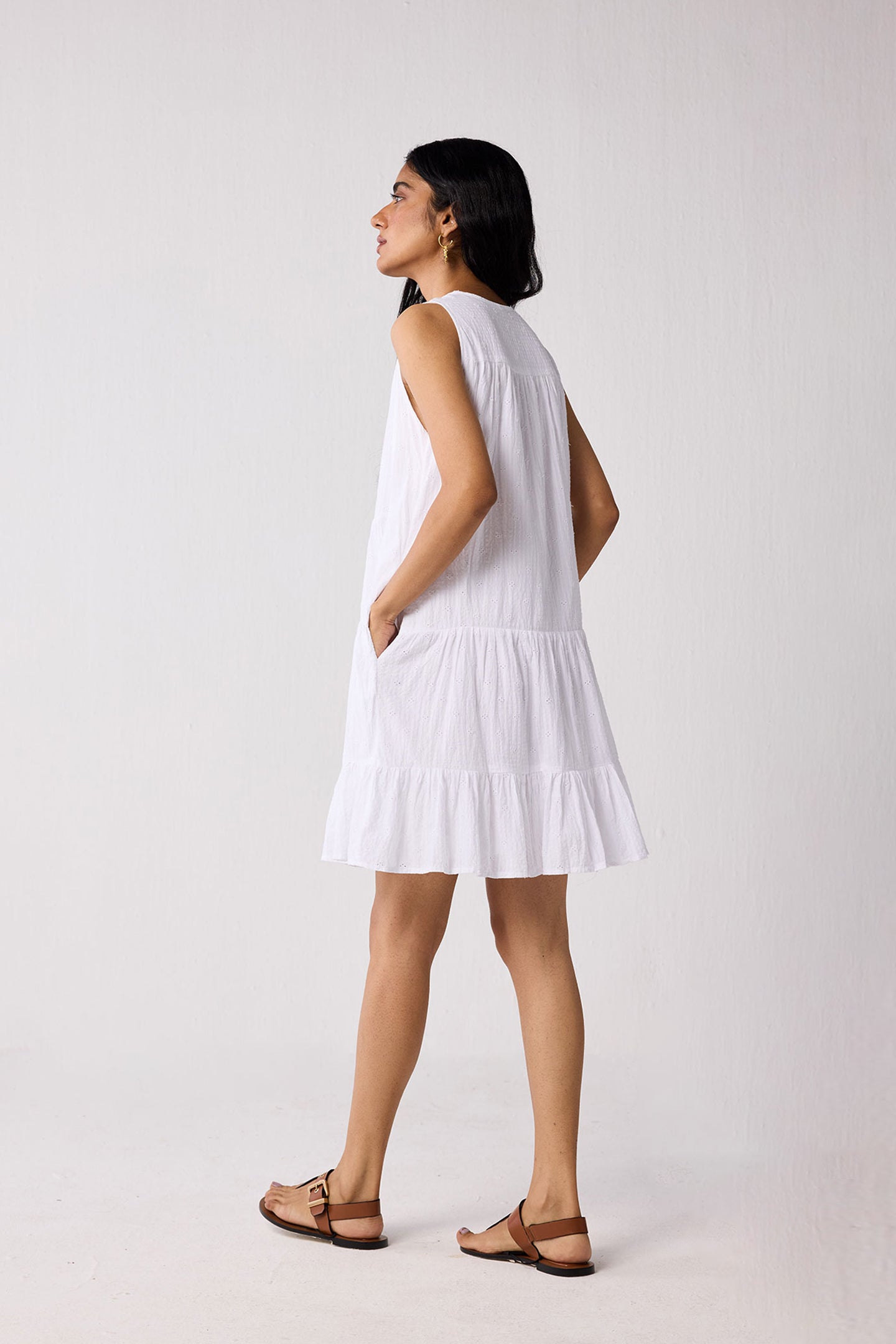 Woman wearing a white dress with cut-out shoulders on a plain background