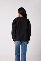 Person wearing a black long-sleeve shirt and blue jeans on a white background