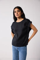 Woman wearing a black top with gathered sleeves and blue jeans on a white background