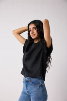 Woman wearing a black top and blue jeans against a plain background