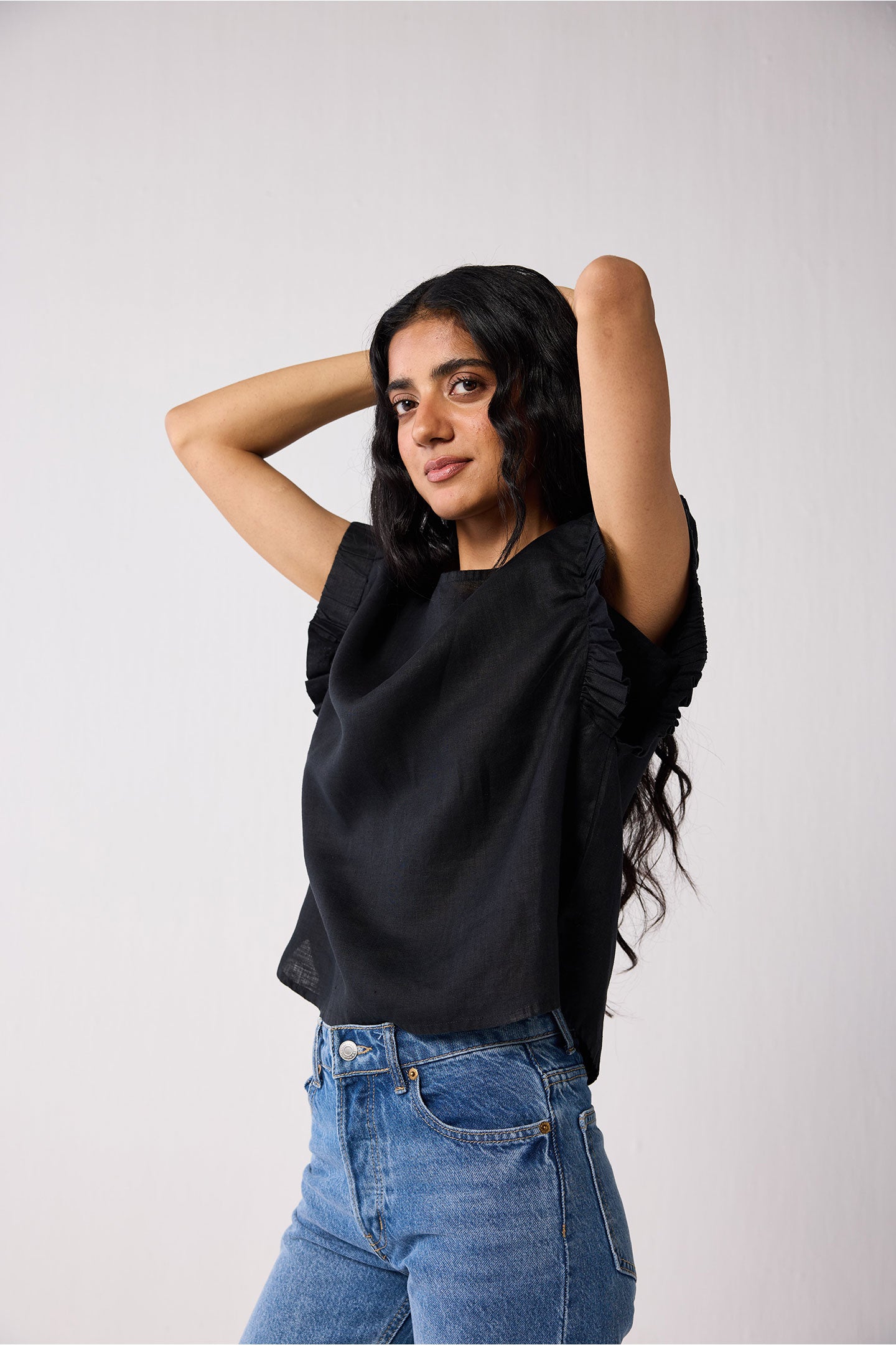 Woman wearing a black top and blue jeans against a plain background