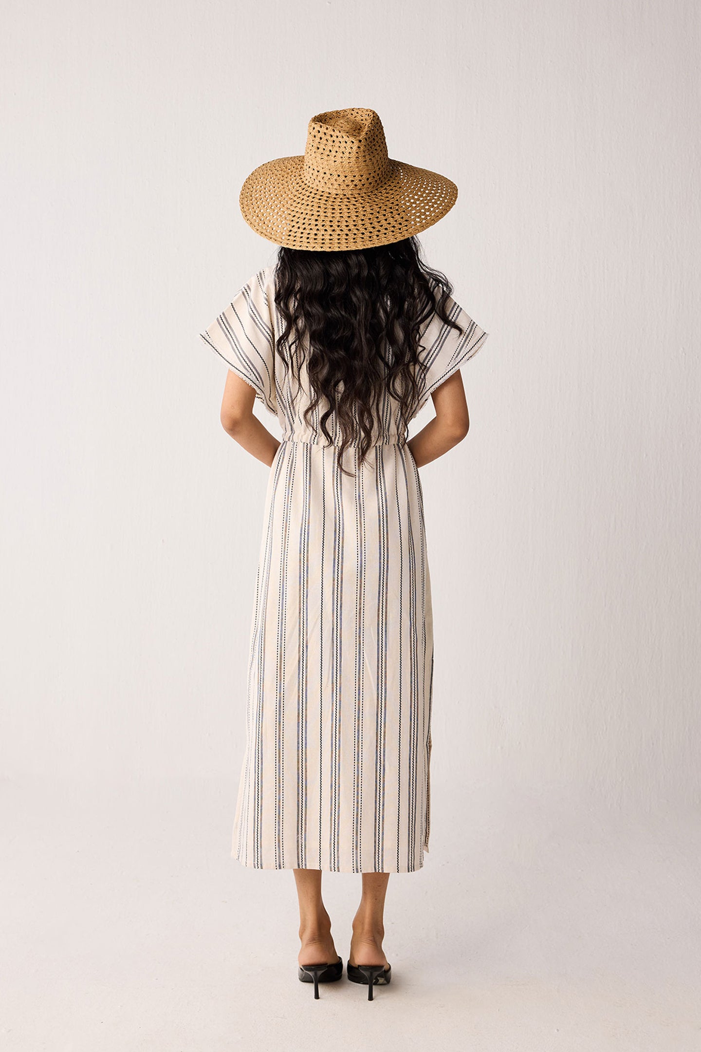 Woman wearing a striped dress and straw hat from behind on a plain background