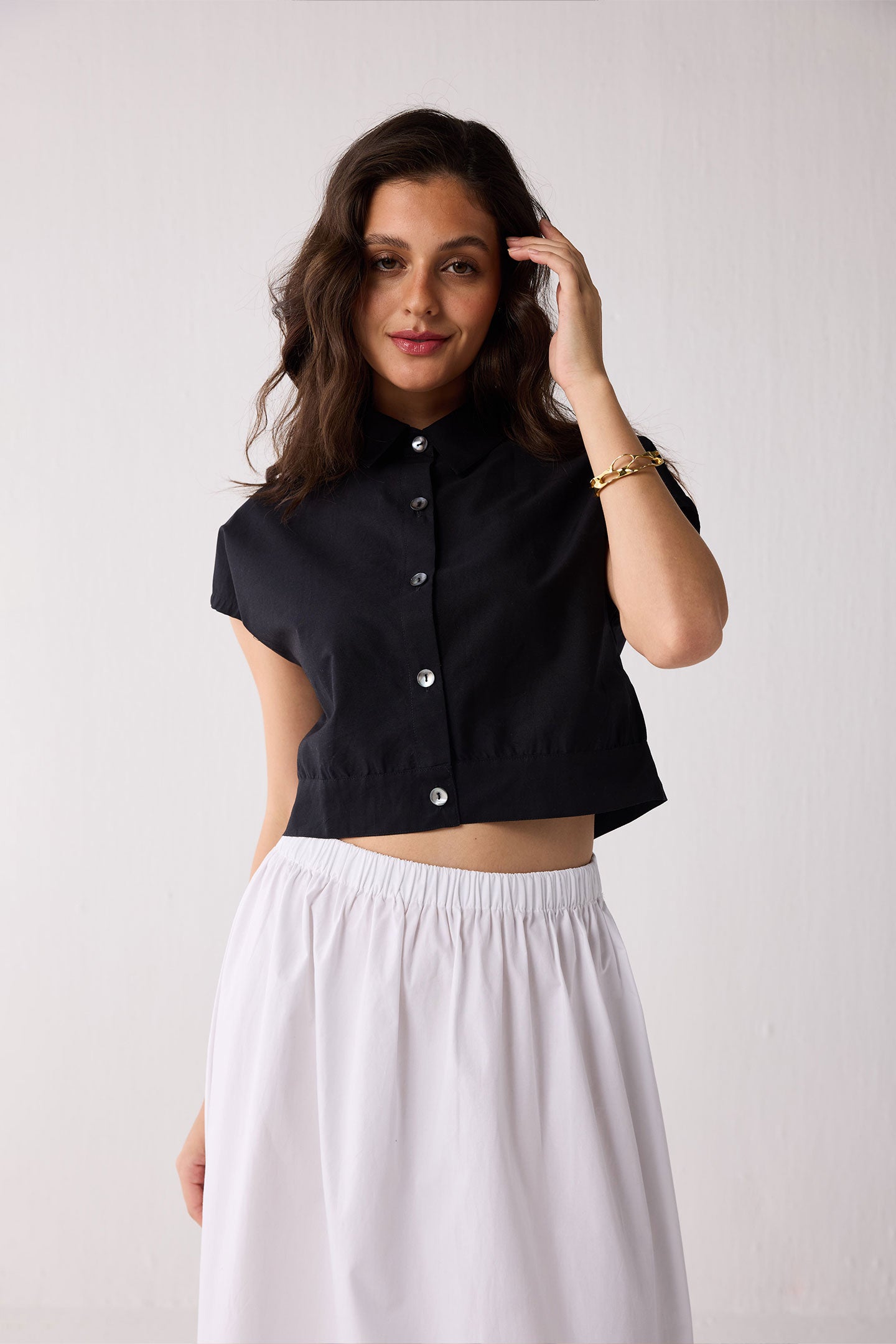 Woman wearing a black cropped top with buttons and a white skirt on a plain background