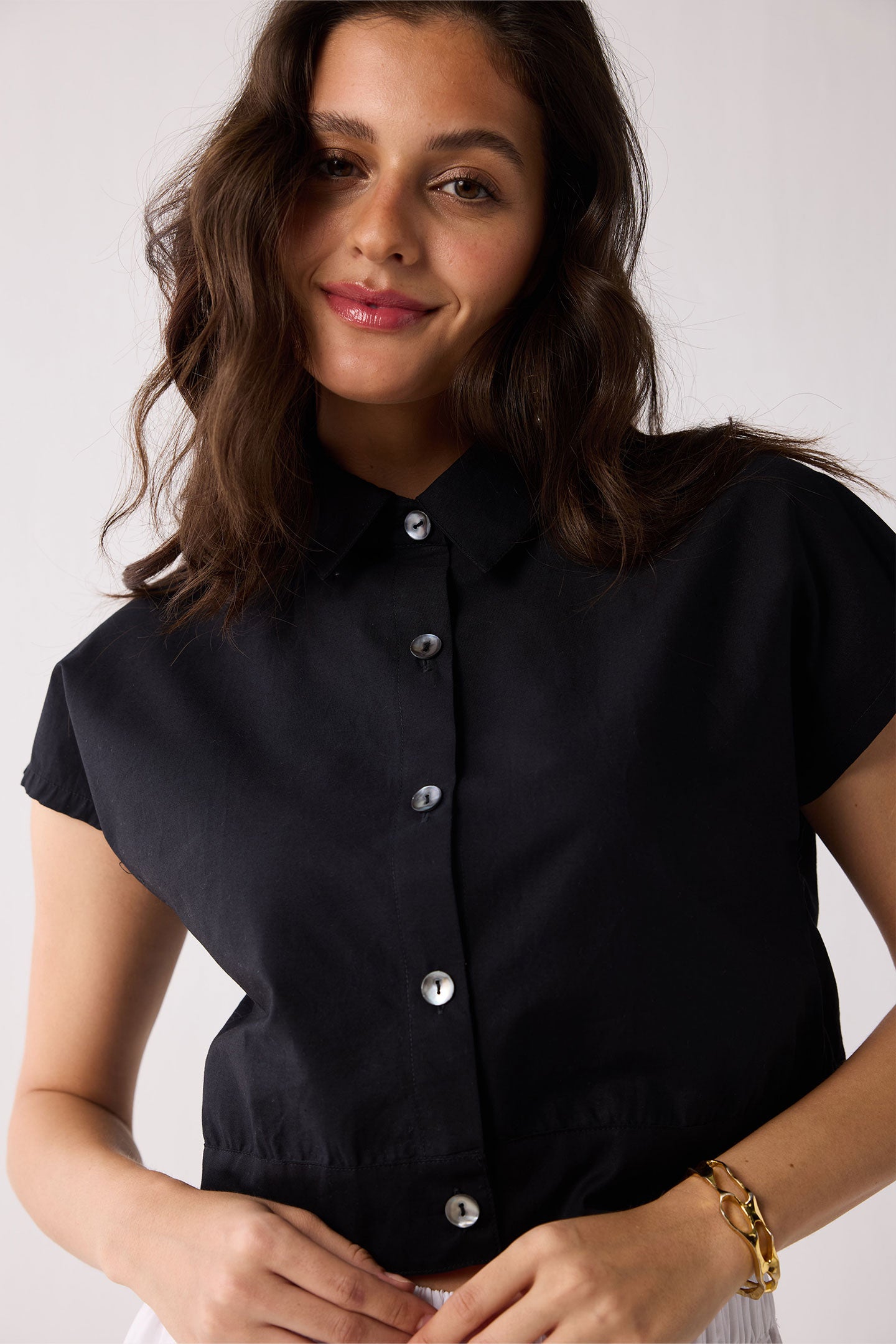 Woman wearing a black short-sleeve blouse with buttons on a white background