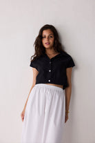 Woman wearing a black short-sleeve top and white skirt against a plain background