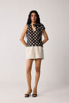 Woman wearing a black sleeveless top with beige polka dots and beige shorts on a white background