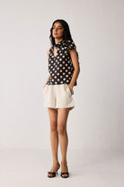 Woman wearing a black sleeveless top with beige polka dots and beige shorts on a white background