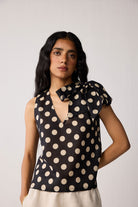 Woman wearing a black sleeveless top with beige polka dots on a white background
