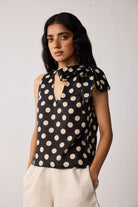 Woman wearing a black sleeveless top with beige polka dots on a white background