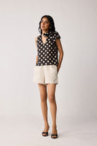 Woman wearing a black sleeveless top with beige polka dots and beige shorts on a white background