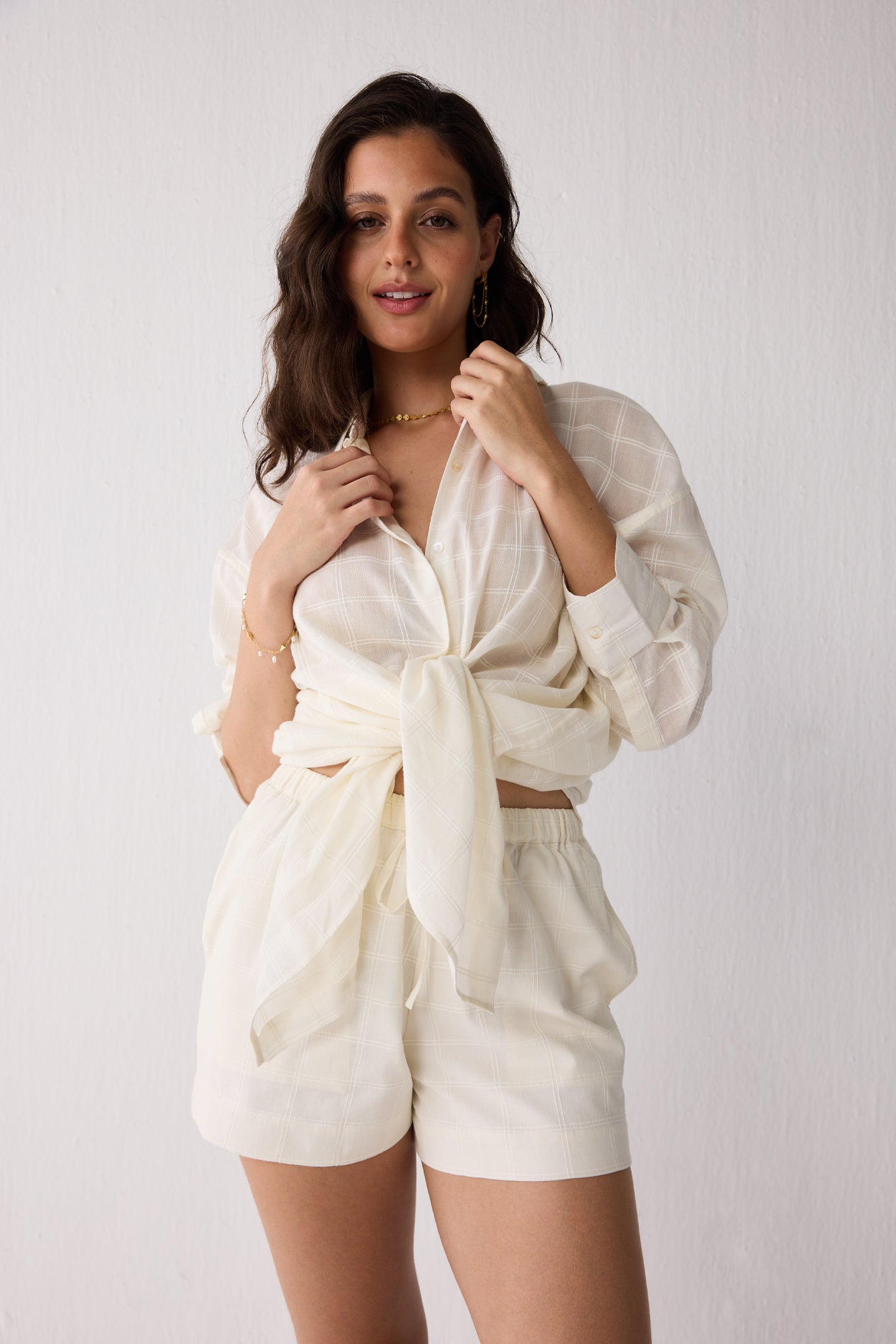 Woman wearing a white outfit with a tied top against a plain background