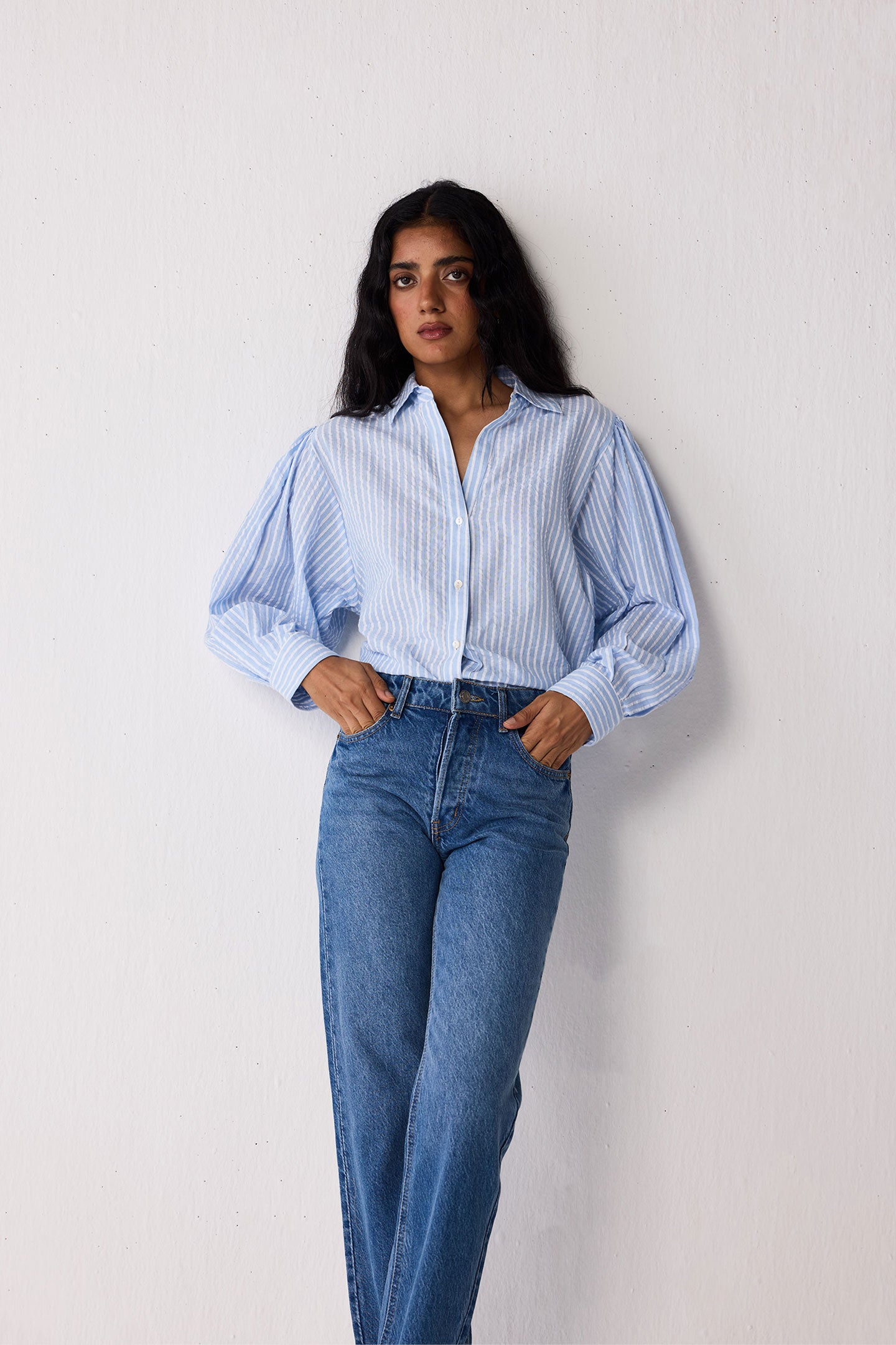 Woman wearing a light blue striped shirt and jeans against a white background
