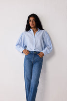 Woman wearing a light blue striped shirt and jeans against a white background