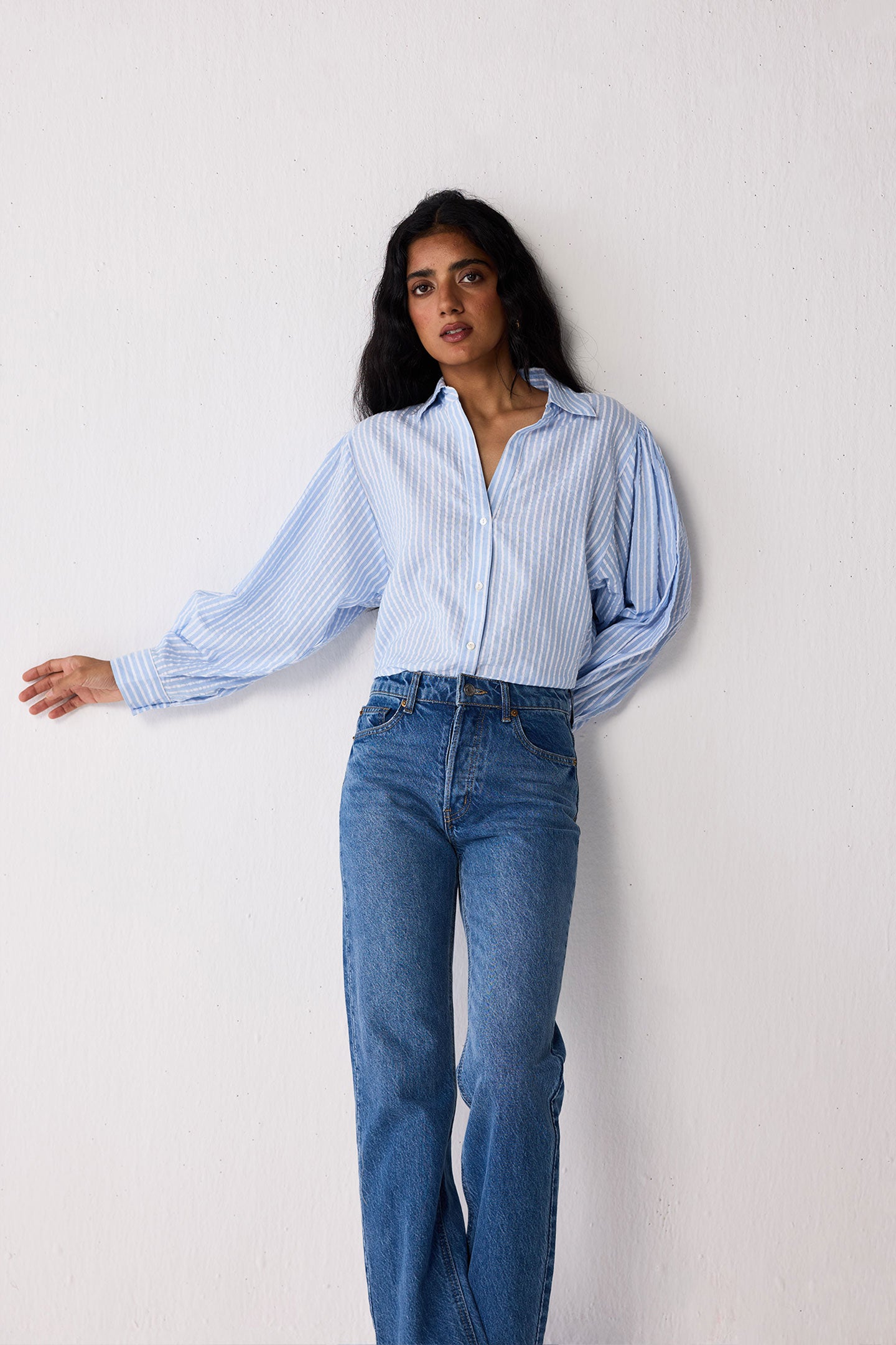 Woman wearing a light blue striped shirt and jeans against a white background